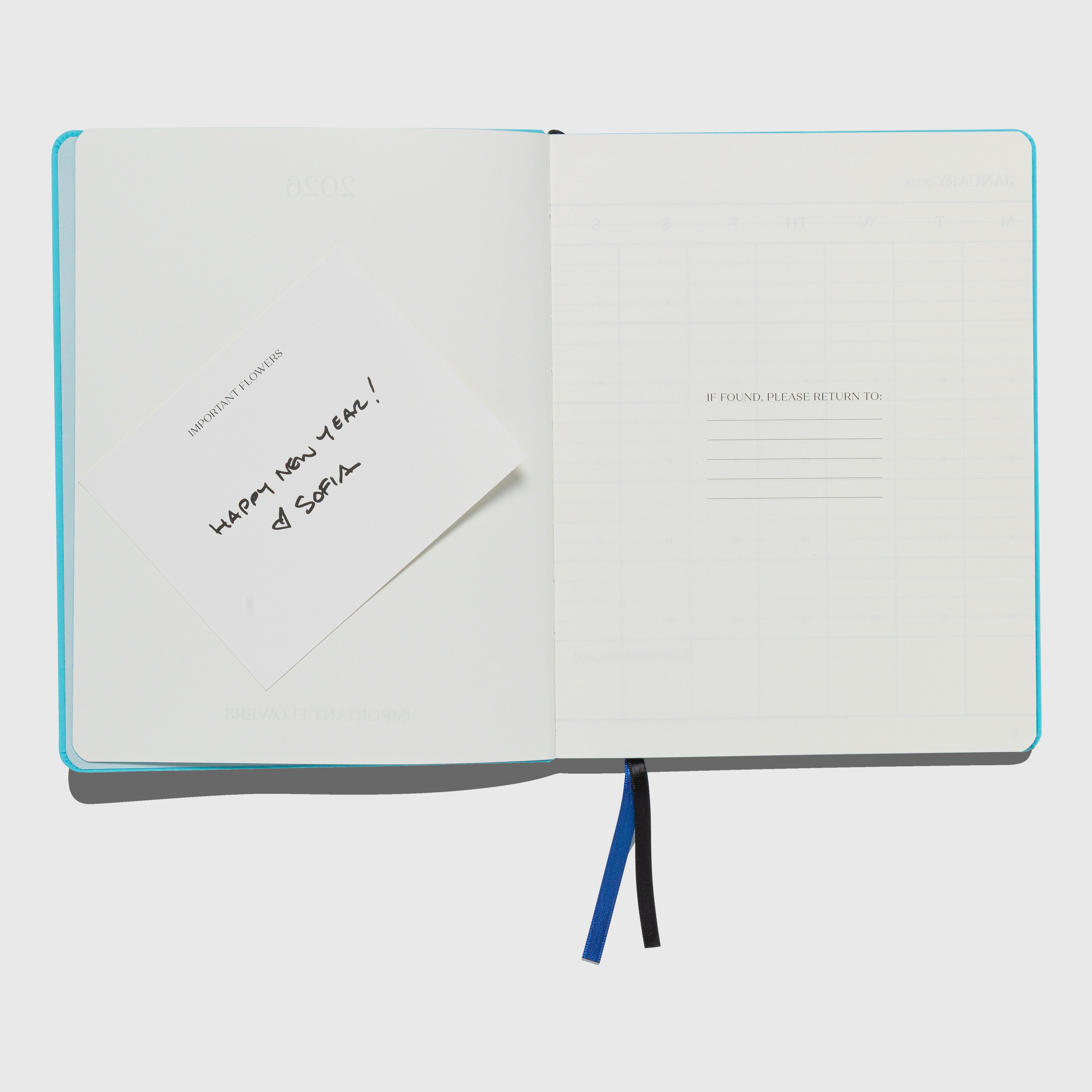 Open notebook with a white cover and blue binding on a light gray background. The Important Flowers 2026 Planner by Sofia Coppola published by Mack.