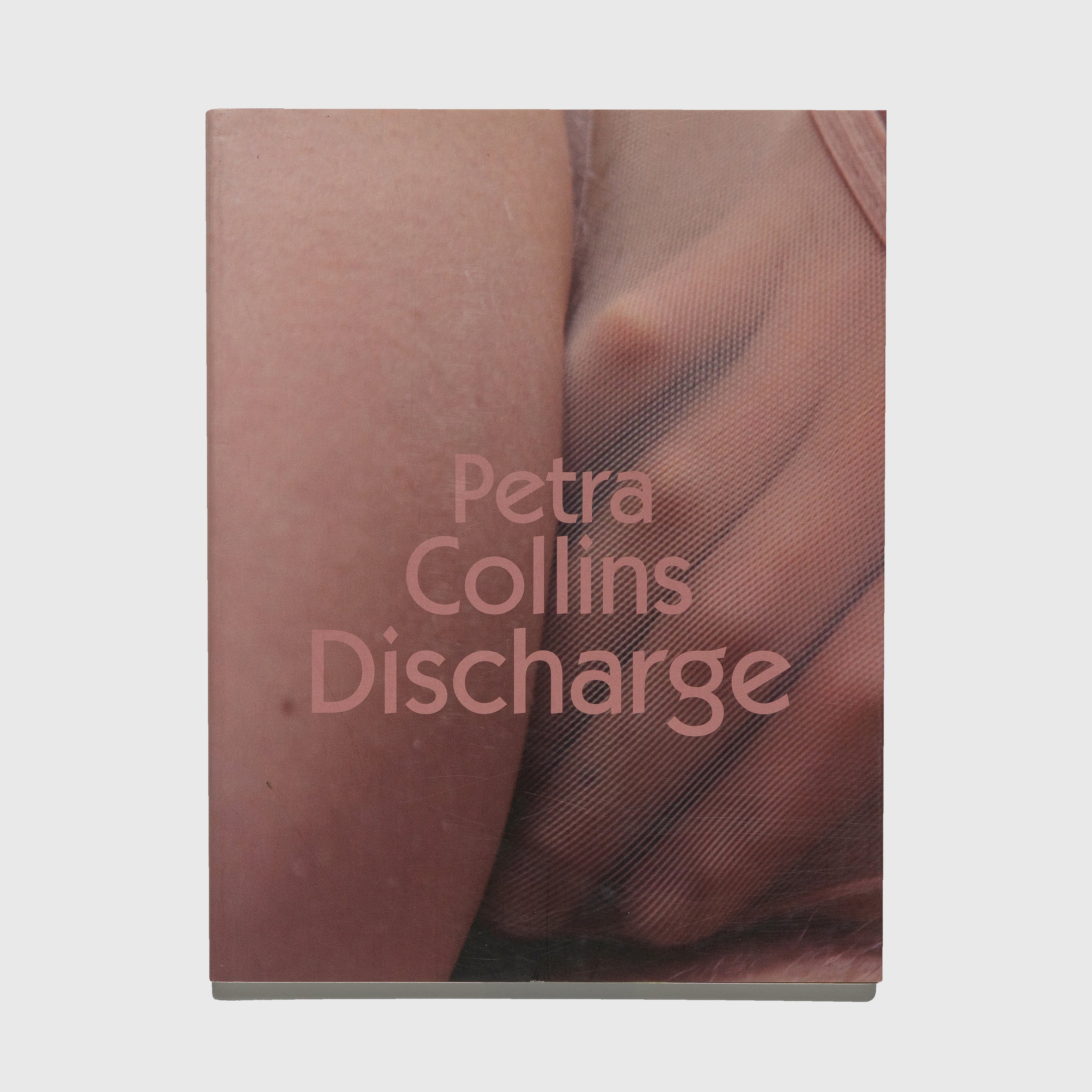 Cover of 'Discharge' photography book by Petra Collins with a close-up of skin and mesh fabric.