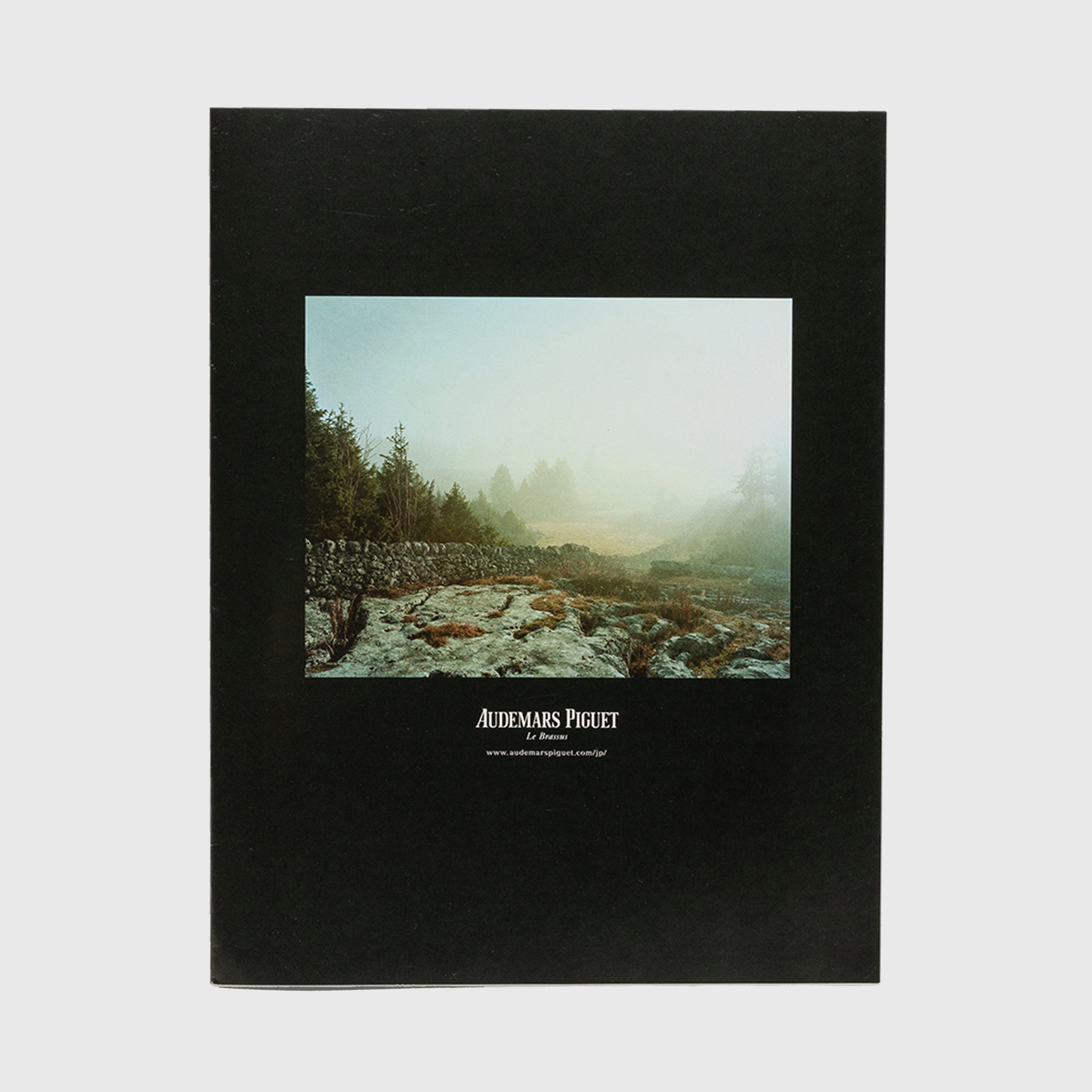 Photograph of a misty landscape with trees and stone wall, featuring Audemars Piguet branding on a magazine cover