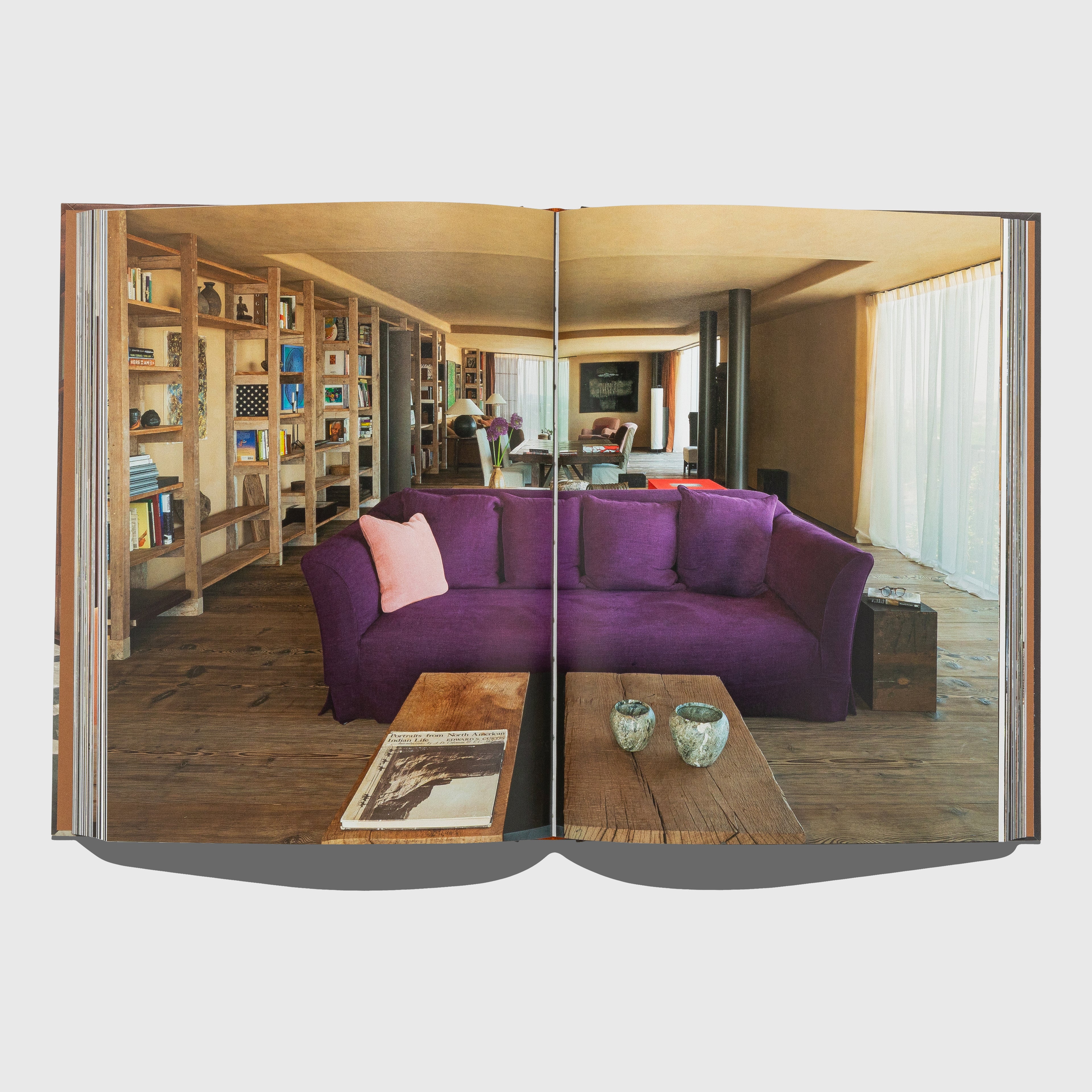 Open book showing a living room with a purple sofa and bookshelf. Portraits of Interiors by Axel Vervoordt published by Flammarion.
