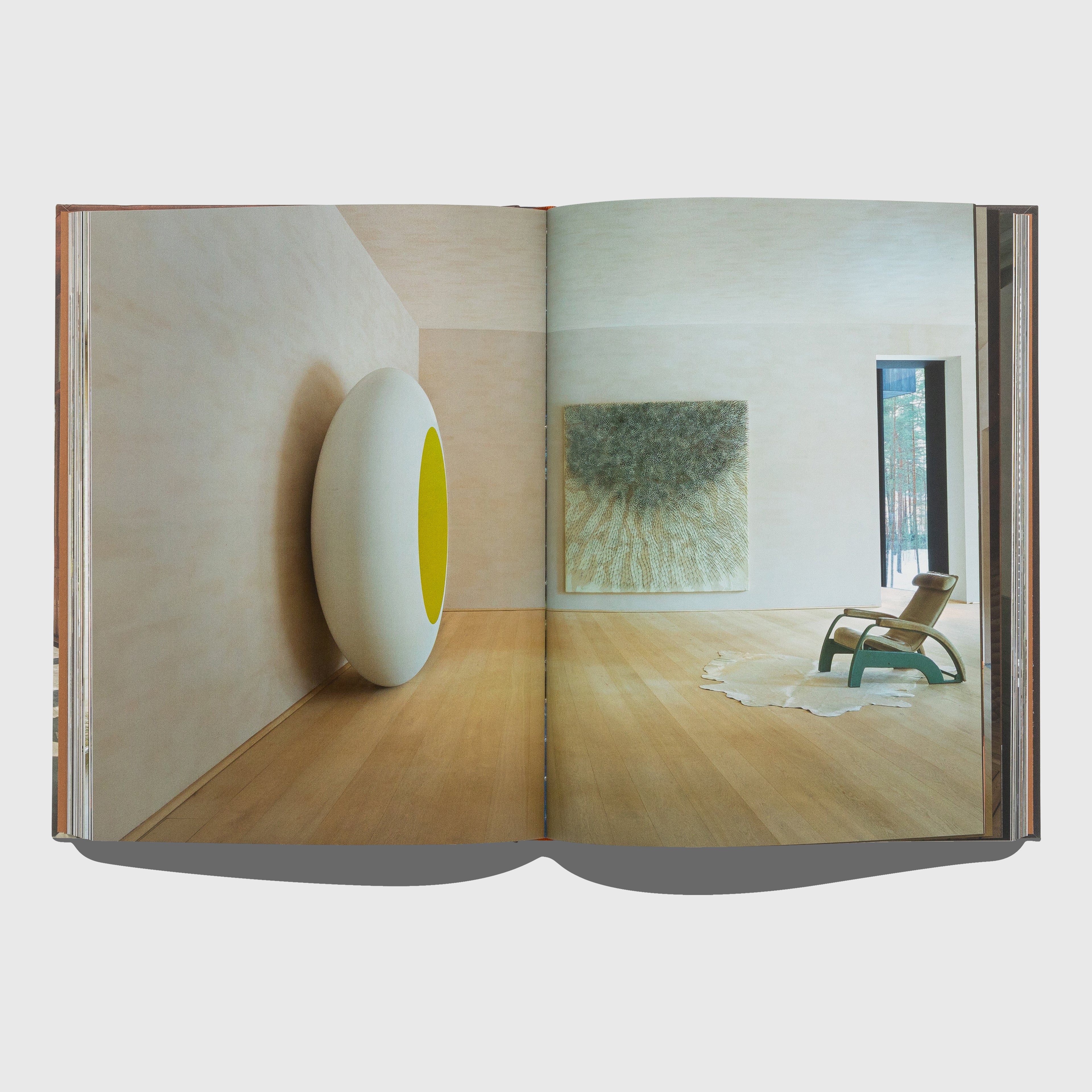 Open book showing a modern interior design with a white wall, round yellow object, and a chair. Portraits of Interiors by Axel Vervoordt published by Flammarion.