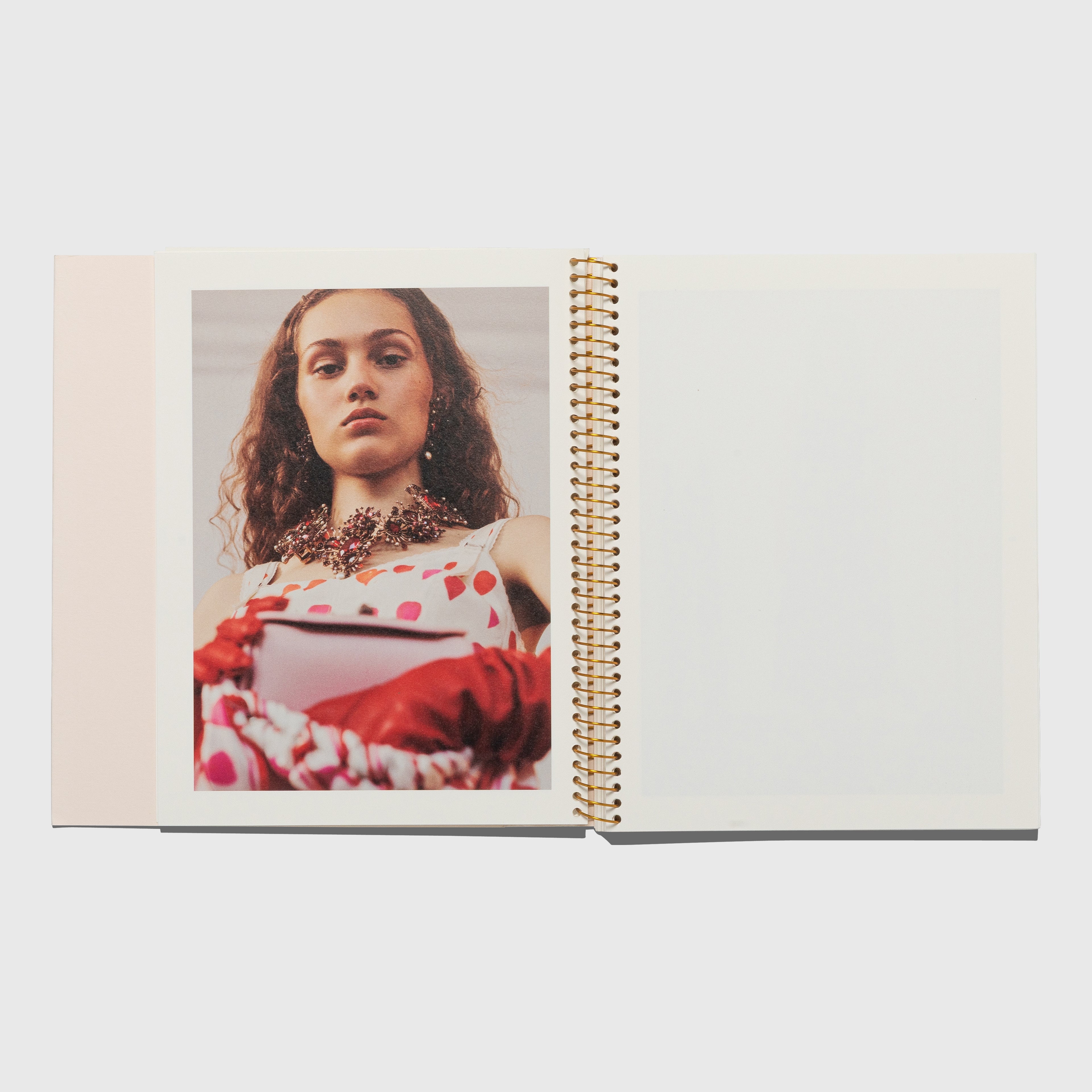Open book with a photo of a person wearing a polka dot dress and necklace on a white background. Alexander McQueen spring summer 2018 catalog